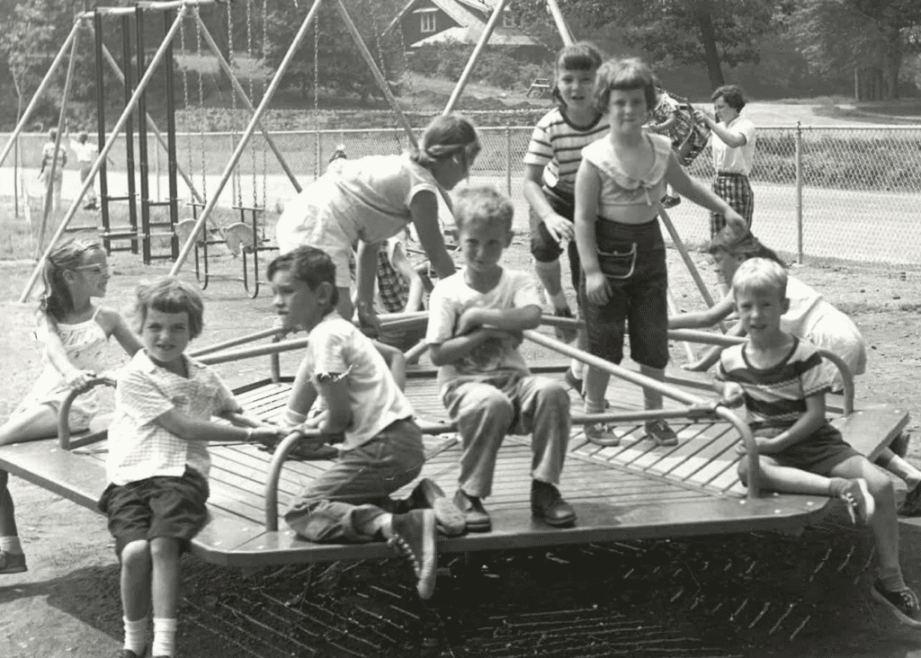 Black and white photo of a group of kids on a merry-go-round.