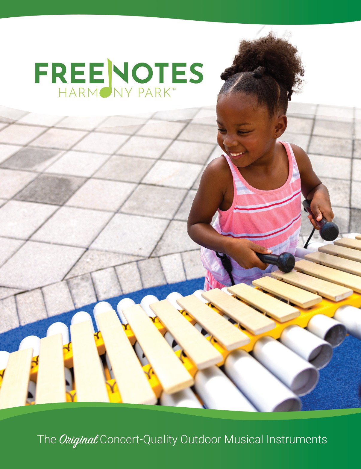 A young girl smiles as she plays a large outdoor xylophone with two mallets on a playground. The image promotes FreeNotes Harmony Park outdoor musical instruments.